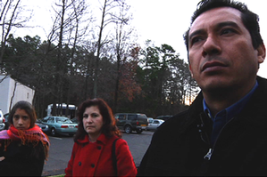 A Latino father, mother and daughter standing in a parking lot.
